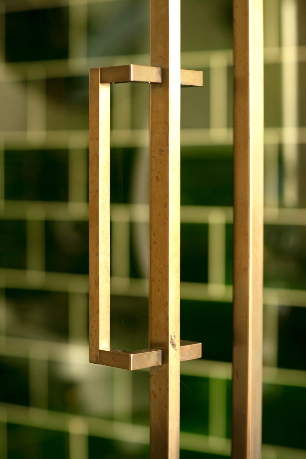 Gold geometric shower door handle with dark tile background