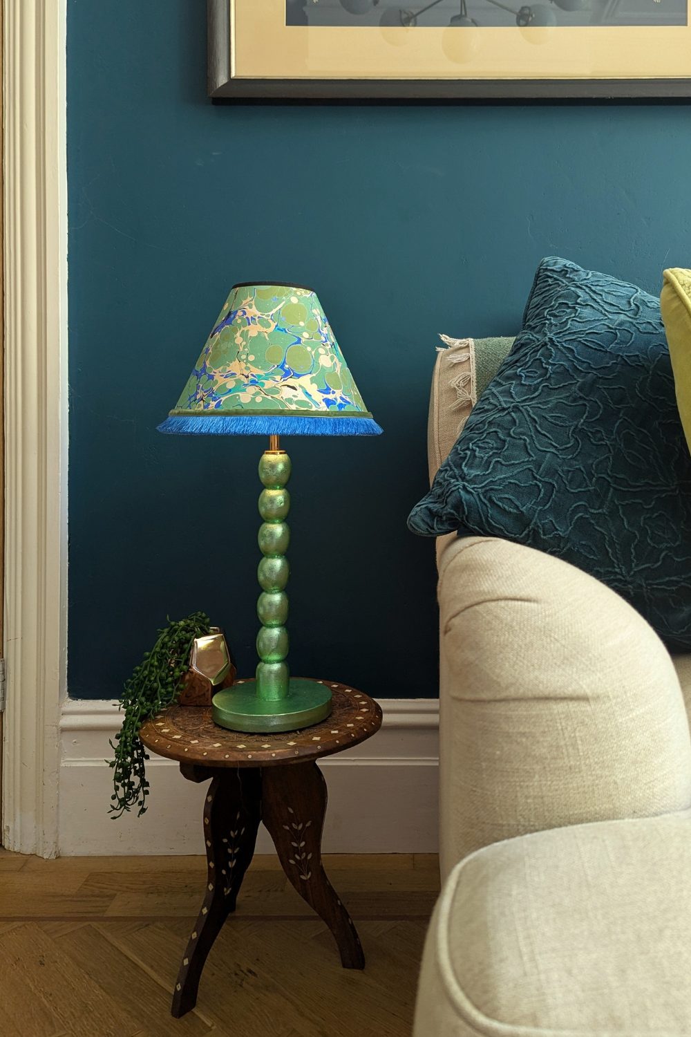 Green lamp on wooden table next to white sofa with blue cushion
