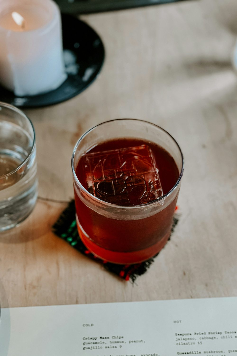 Whisky glass with ice on wooden table next to white candle