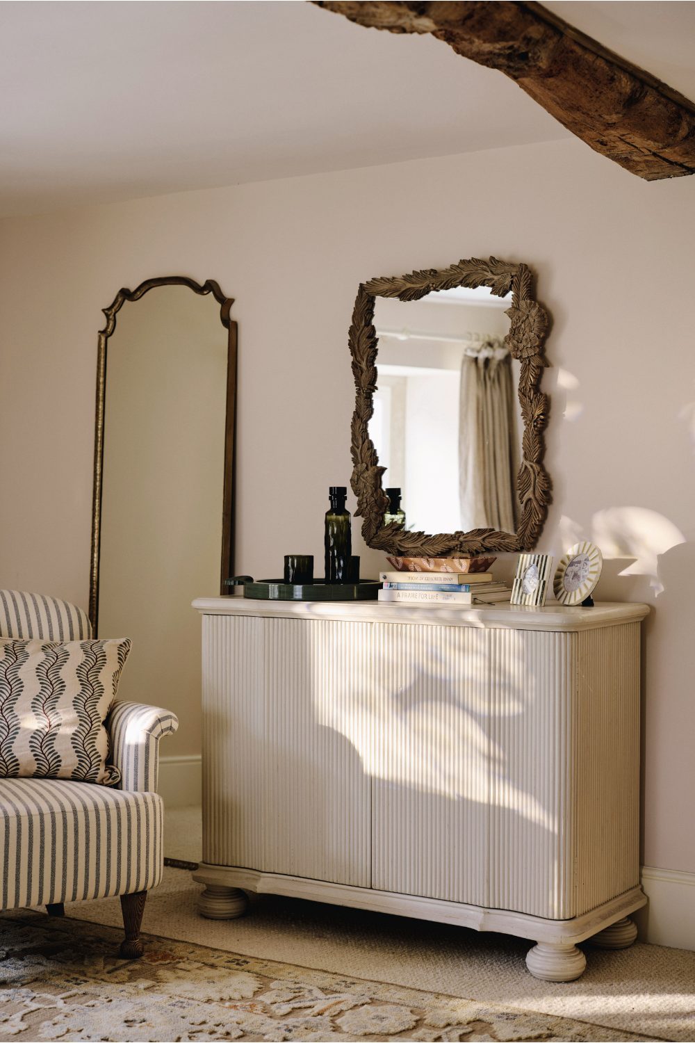 White cabinet and wooden-framed mirror next to white and blue striped armchair on patterned rug