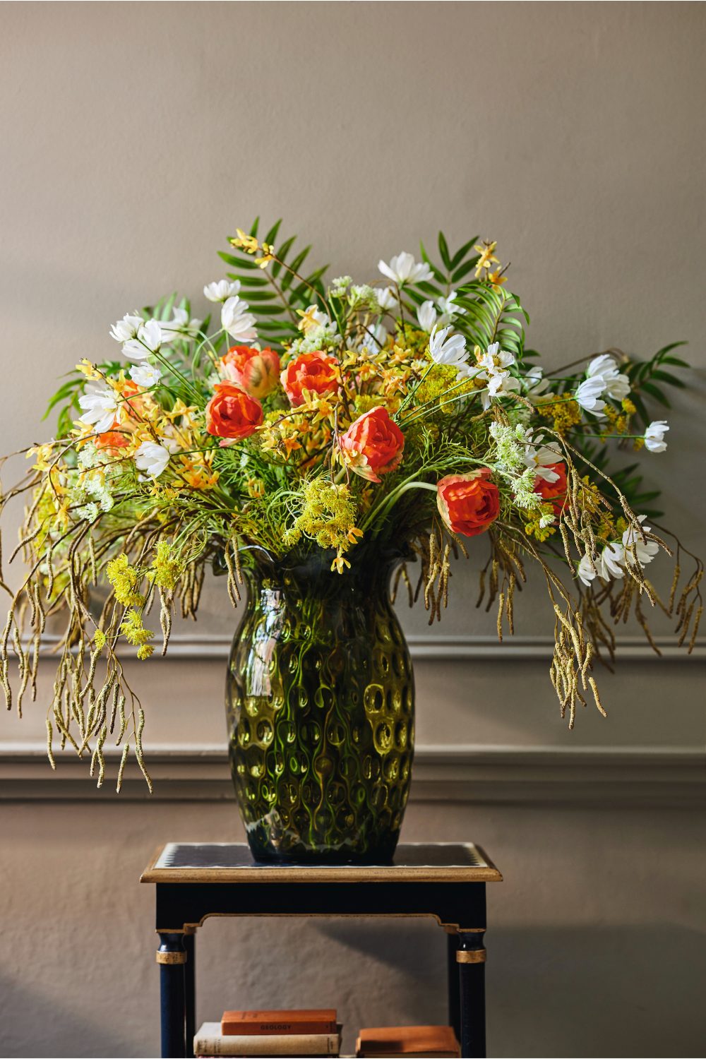 Green vase on black table holding greenery and orange and white flowers 