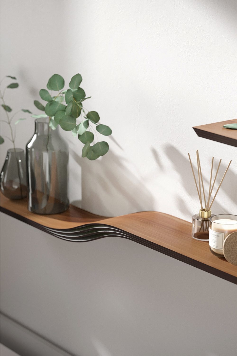 Curved wooden shelf on white wall holding candle and glass vases with greenery