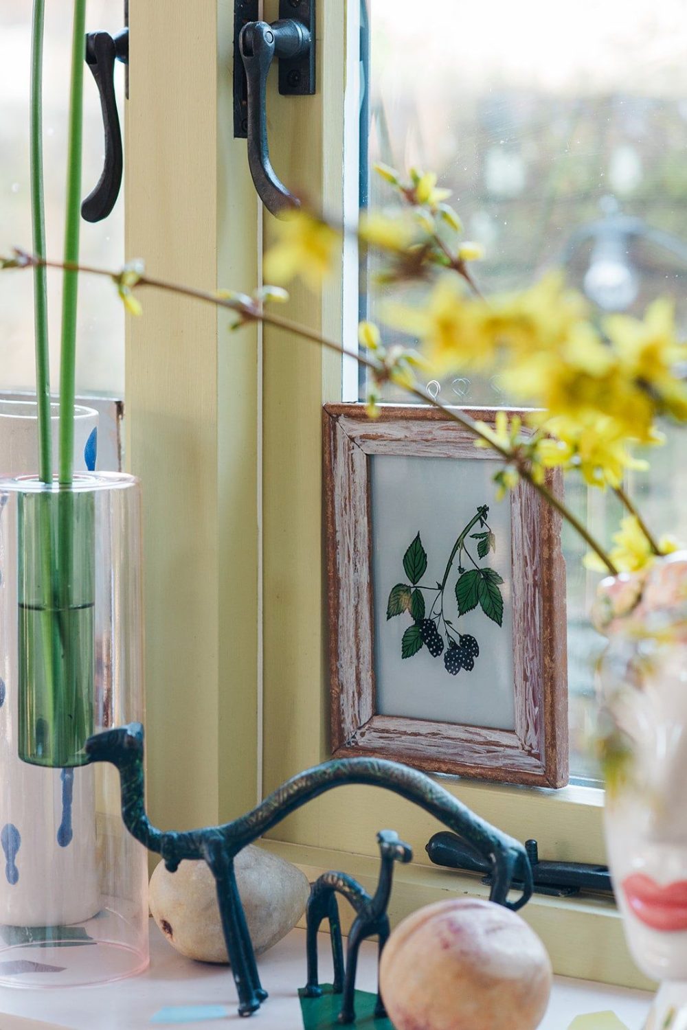Window sill holding wooden-framed botanical picture, black metal animal sculptures, and vases