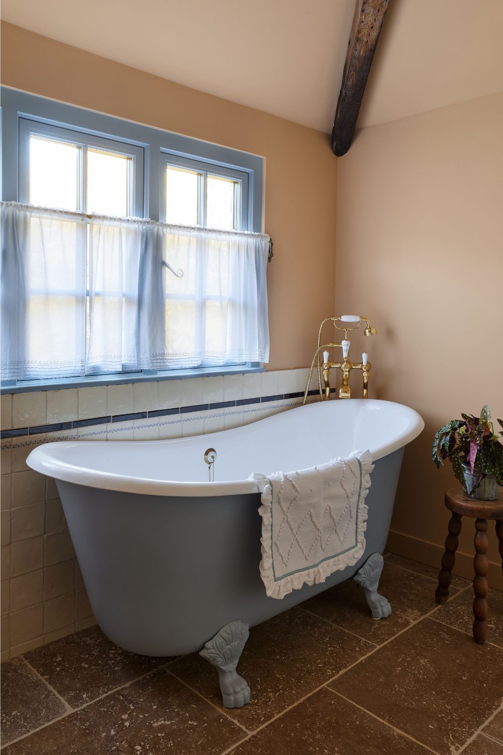 Freestanding blue bathtub with claw feet on stone tile floor in front of blue window