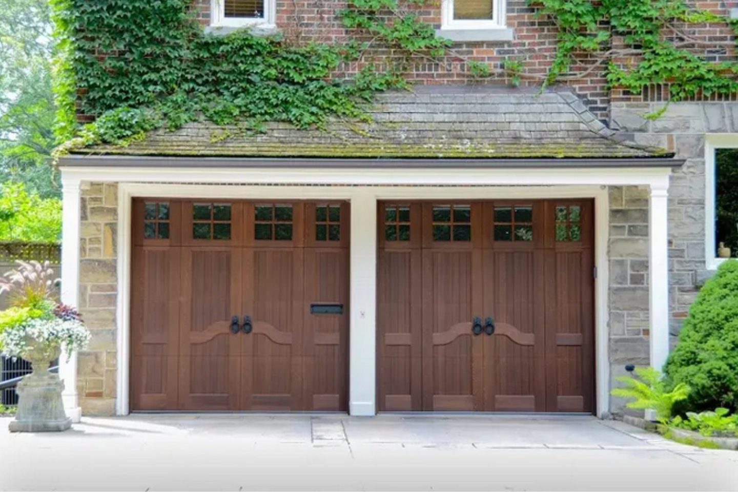 Ivy-covered garage with two large wooden doors with garden around driveway