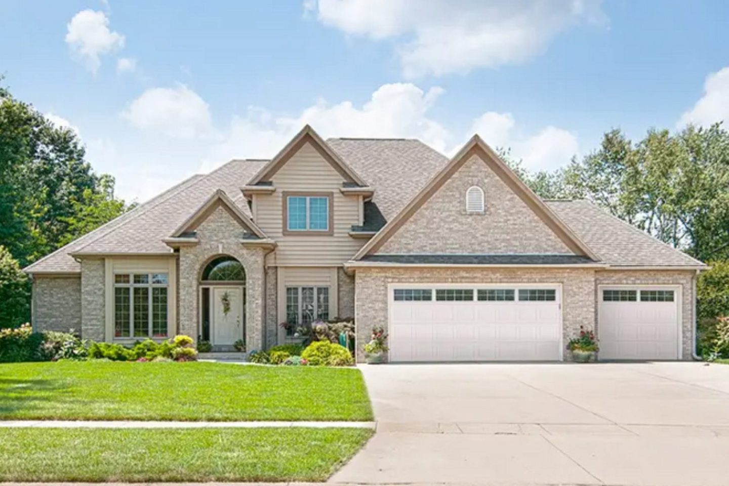 Large grey brick house with white garage and lawn