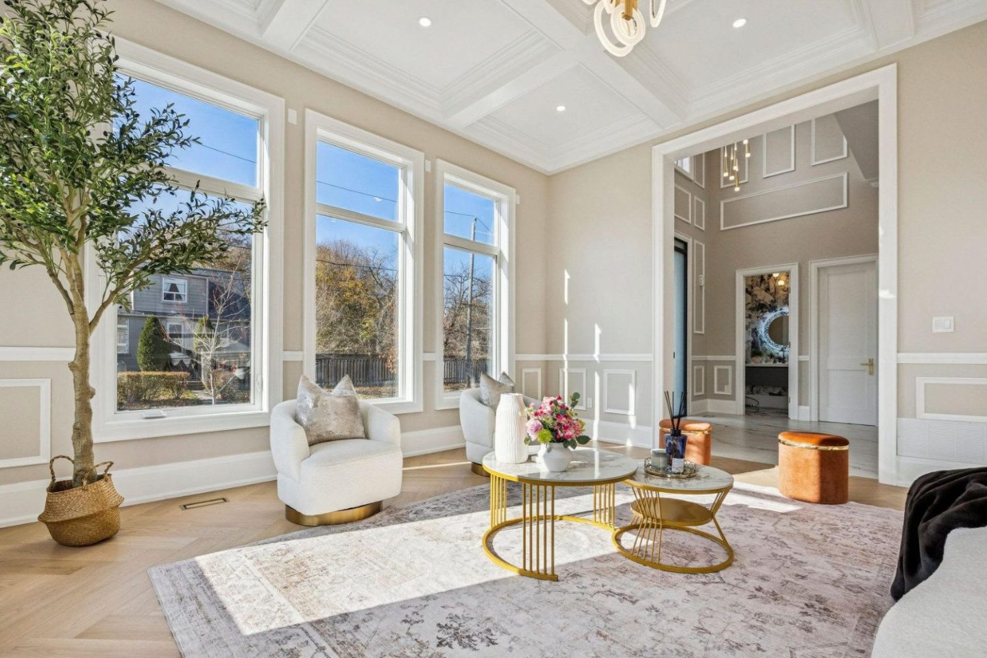 Large white living room with white armchairs, rug, orange pouffes, potted tree and gold table.