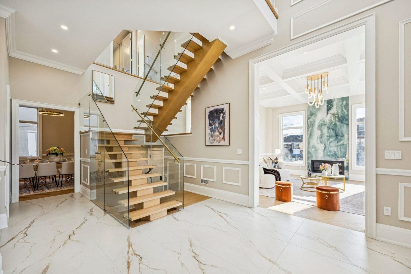 Landing space with white marble floor, wooden stairs and view into living room with orange pouffes
