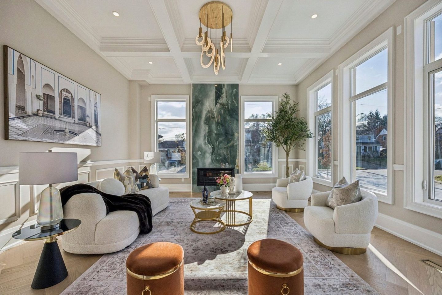 Large white living room with white armchairs and sofa, rug, orange pouffes, potted tree and gold table.
