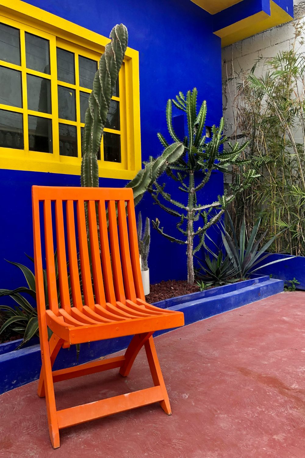 Courtyard with orange folding chair, blue wall, yellow window and cacti bed