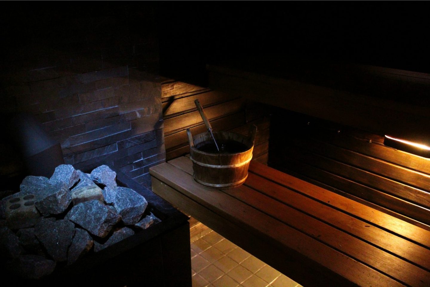 Wooden benches and bucket next to pile of stones inside a sauna