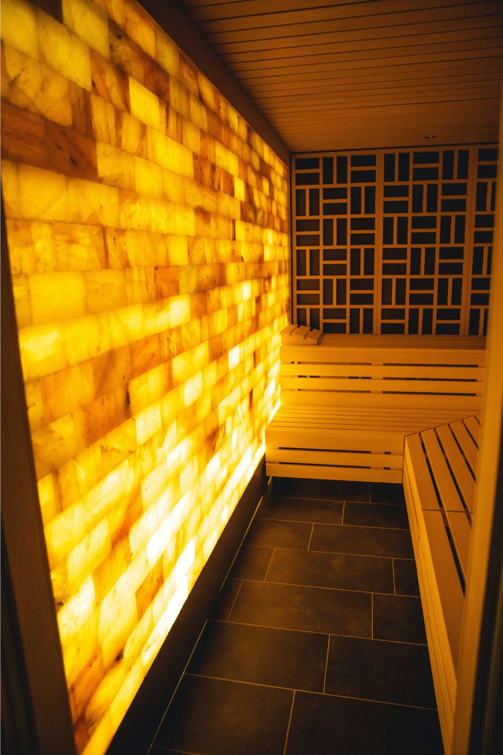 Wooden benches inside sauna below decorative wooden tiling and illuminated yellow brick wall