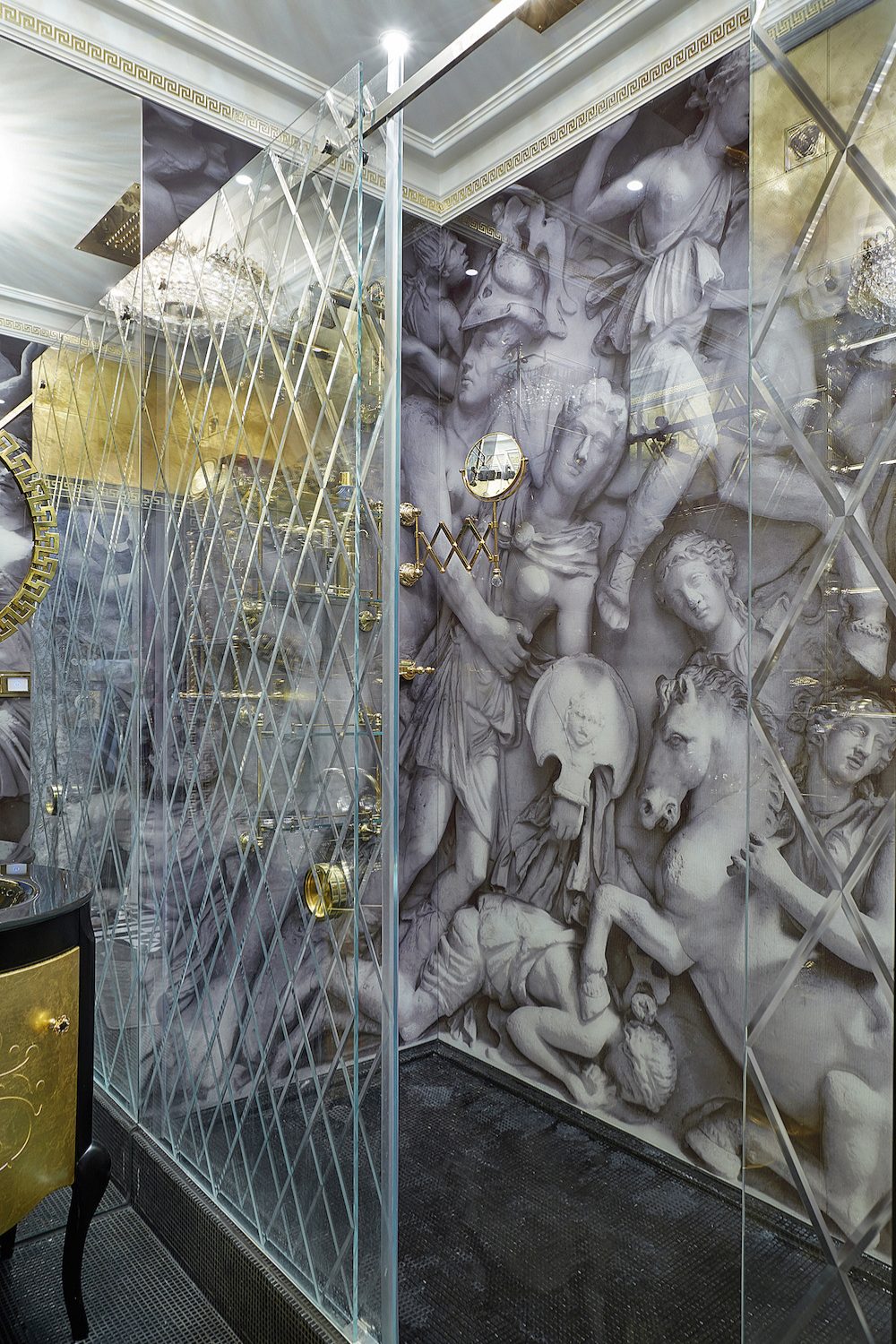 Shower cubicle with cross-hatched glass doors, gold hardware, and classical statue design on walls