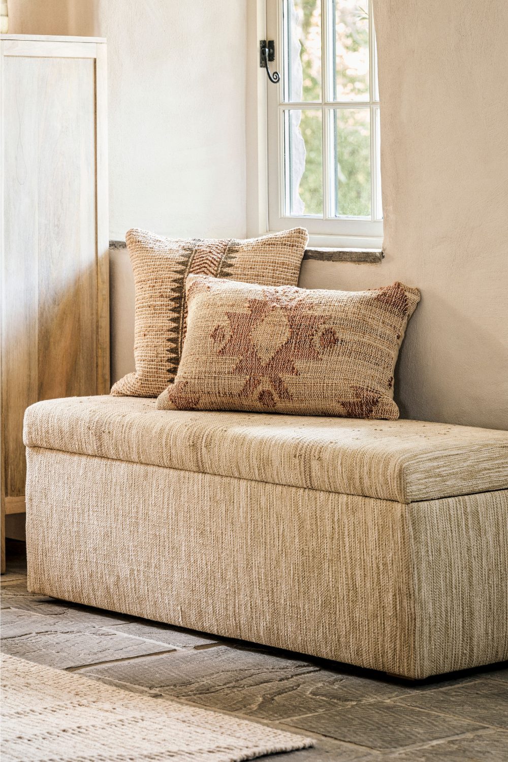 Neutral storage bench with cushions on stone floor with jute rug