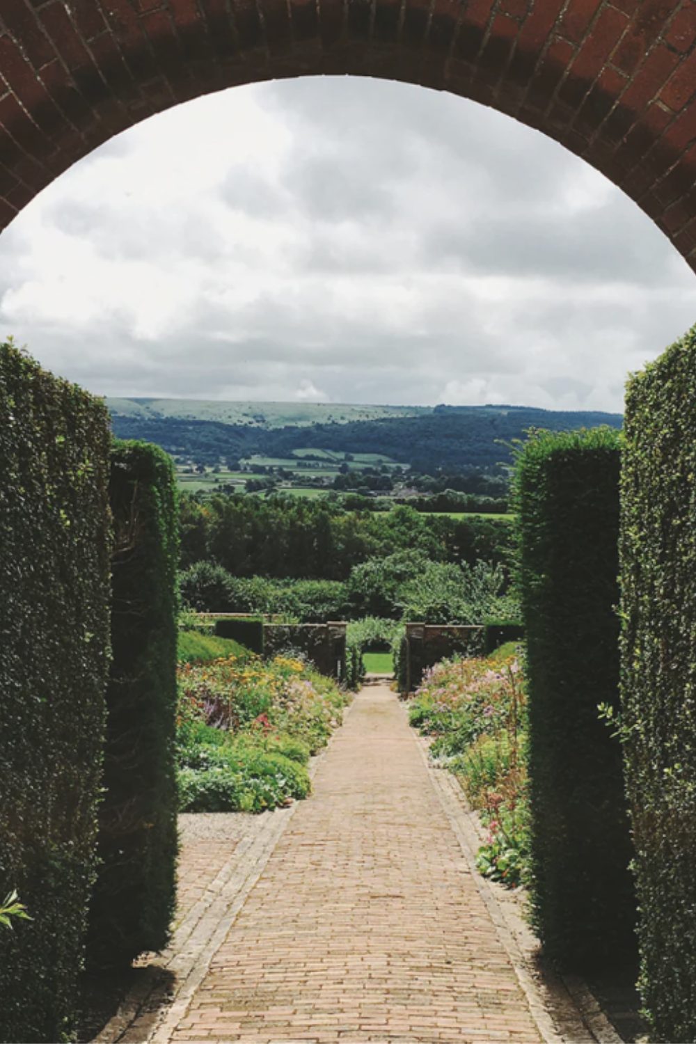 Brick arch framing a countryside view, hedges and tiled path