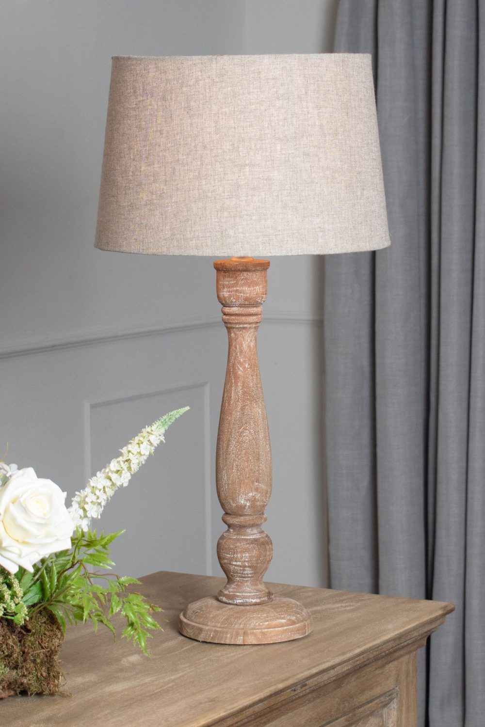 Wooden lamp and white flowers on wooden sideboard by grey curtains