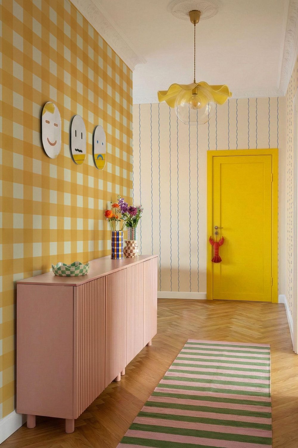 Bright hallway with wooden floor, yellow door, yellow lampshade, patterned wallpaper, pink cabinet and pink & green rug