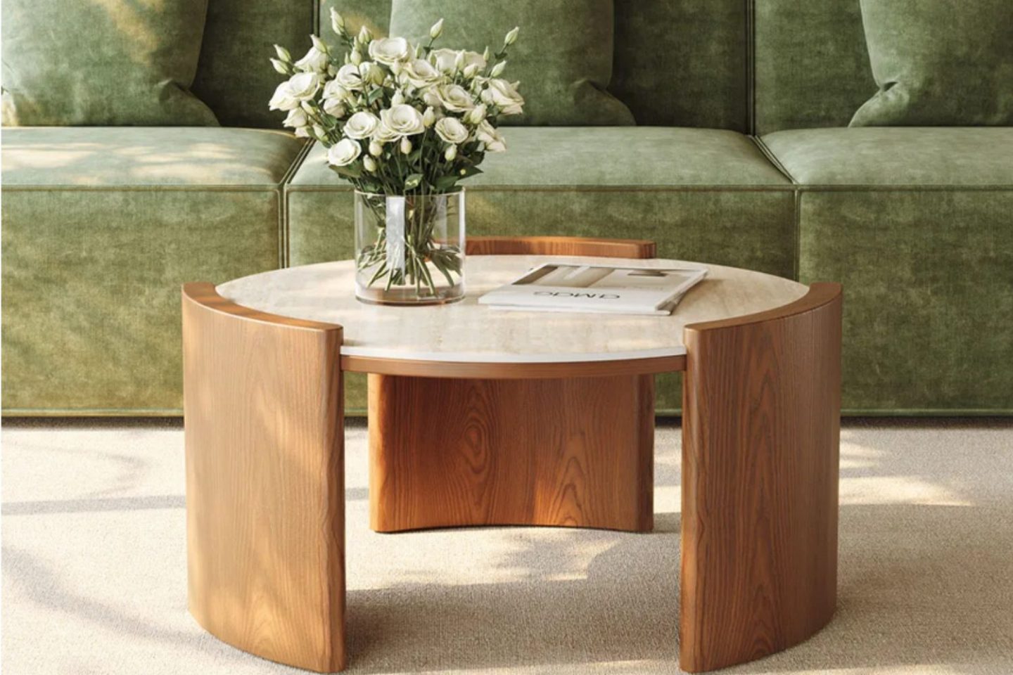 Round wooden and stone coffee table holding vase of white flowers in front of green sofa