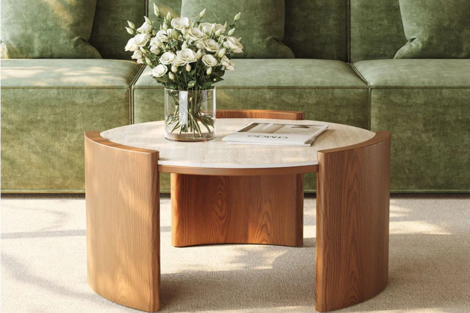 Round wooden and stone coffee table holding vase of white flowers in front of green sofa