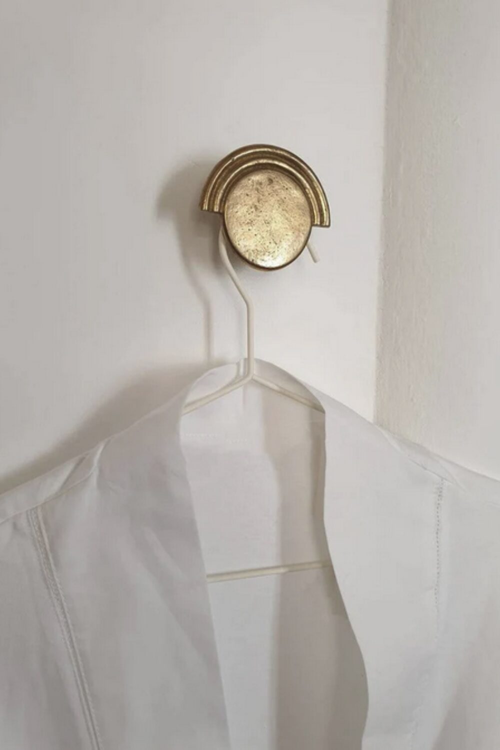 White shirt hanging on round brass hook on white wall