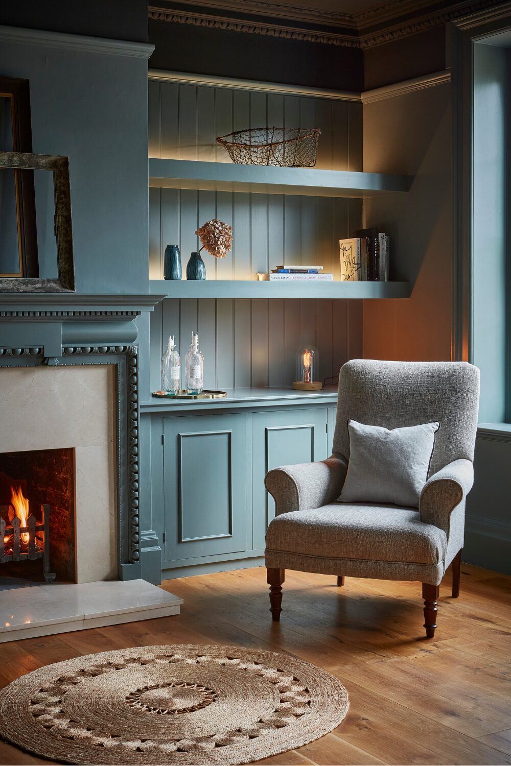 Blue chair in front of fireplace, round rug, and built-in blue shelves holding books and vases