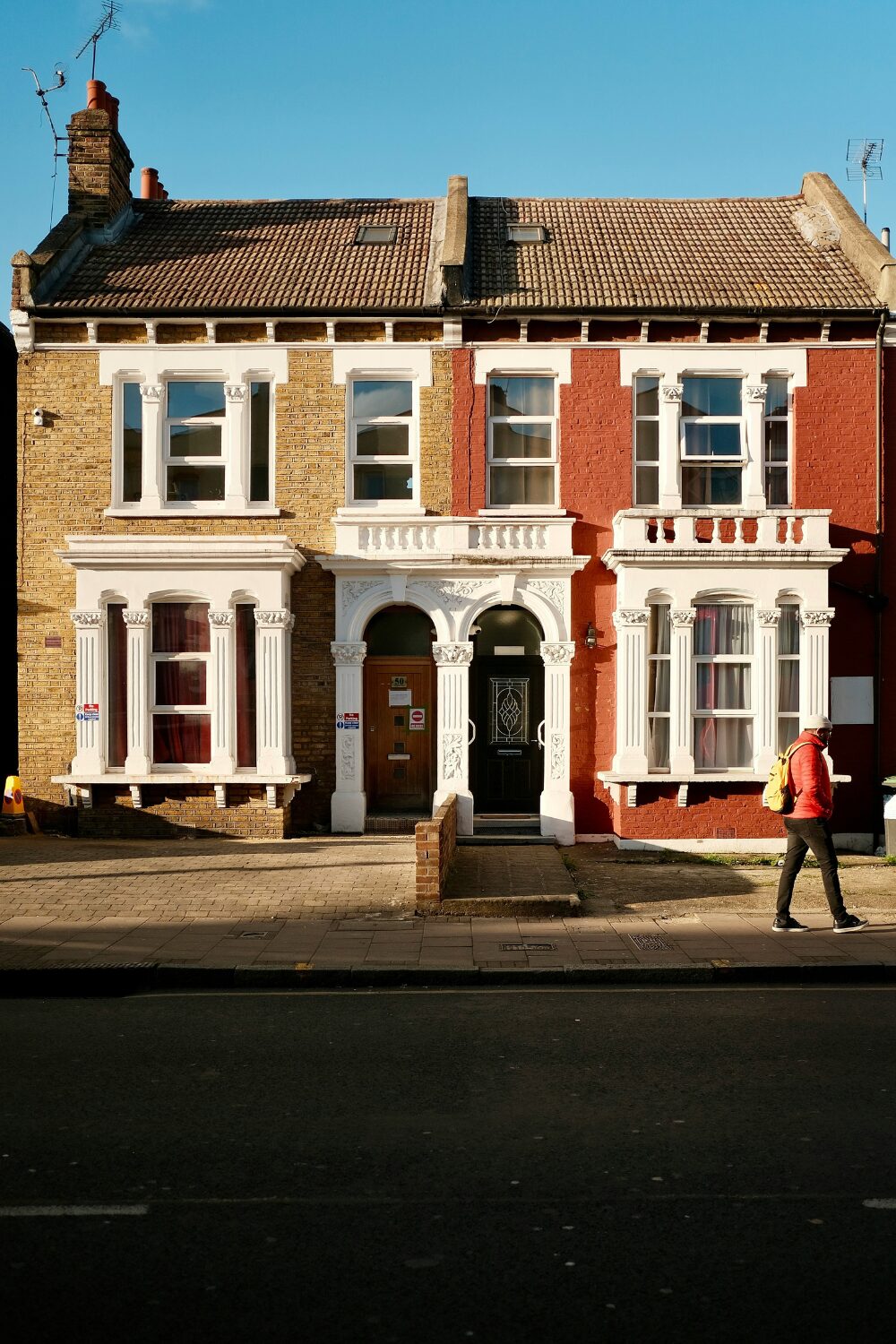 Man walks past a double-fronted brick house with casement windows, and white pillar arches around doors