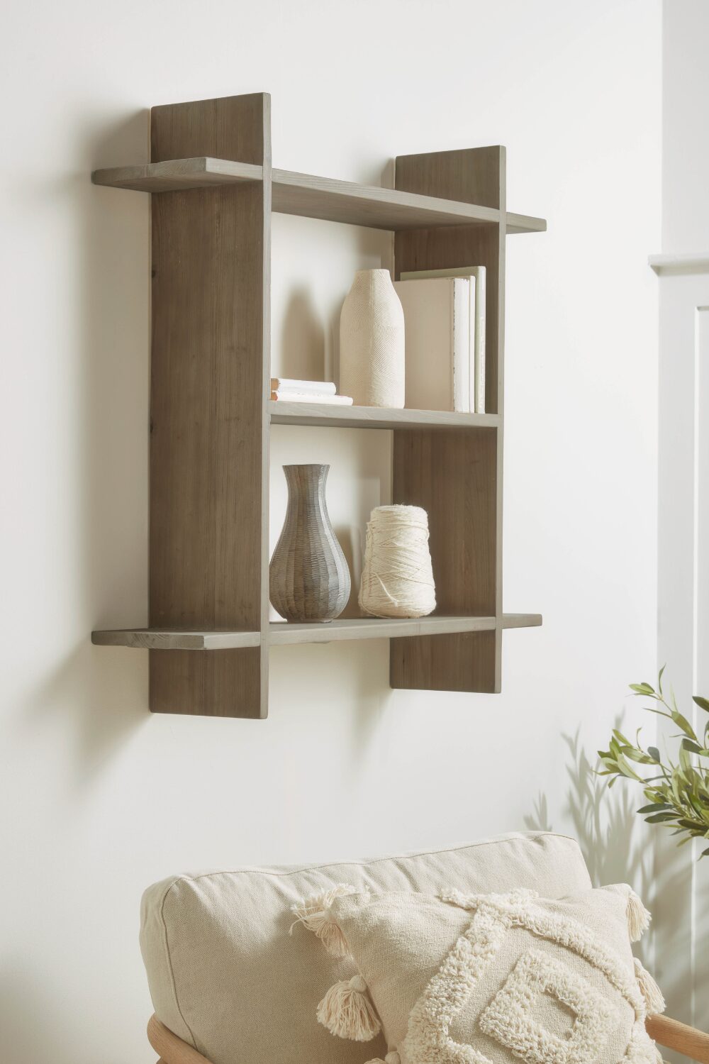 Grey shelving unit holding white vases and books above white chair