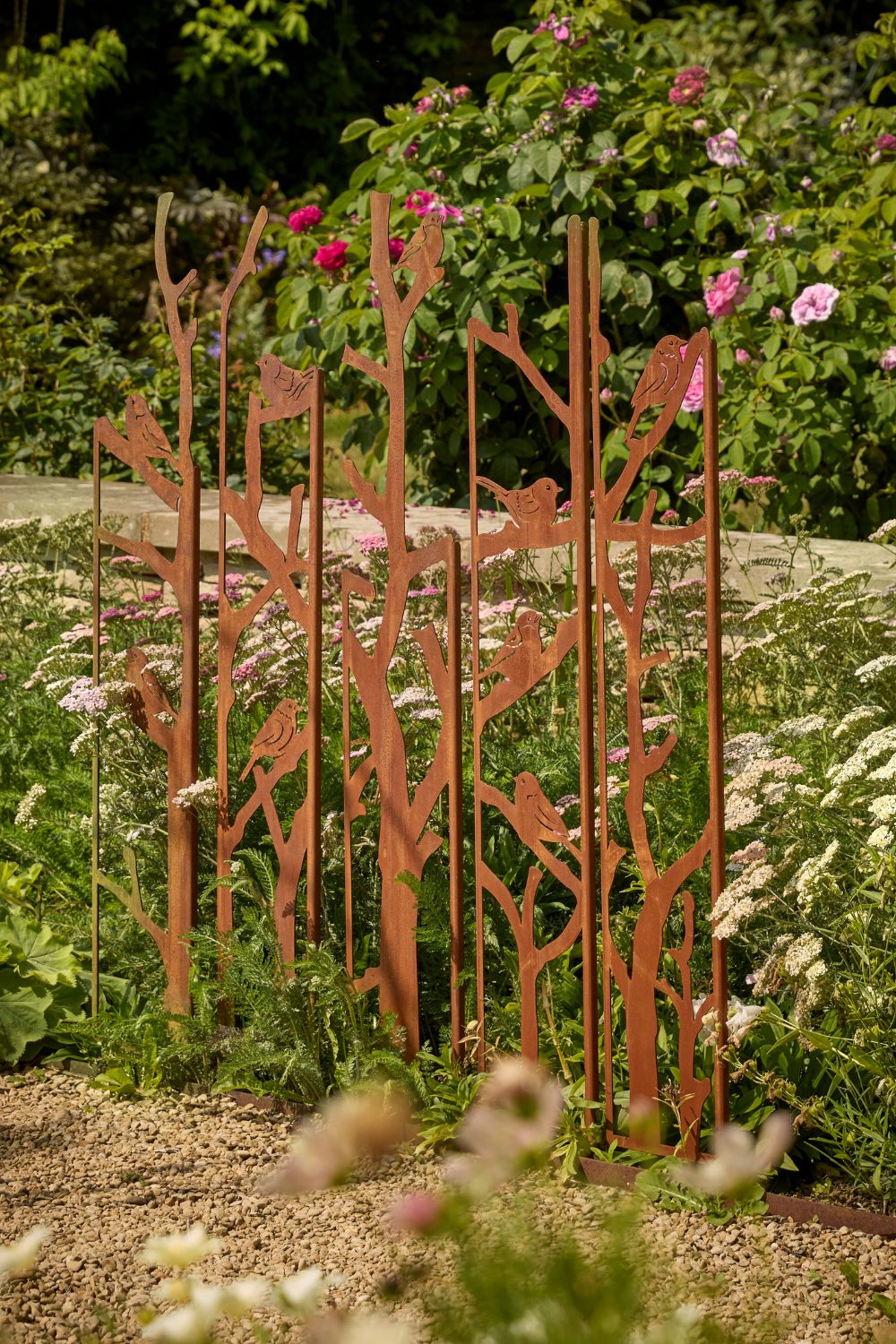 Metal trellis with bird design in white flowers next to gravel path