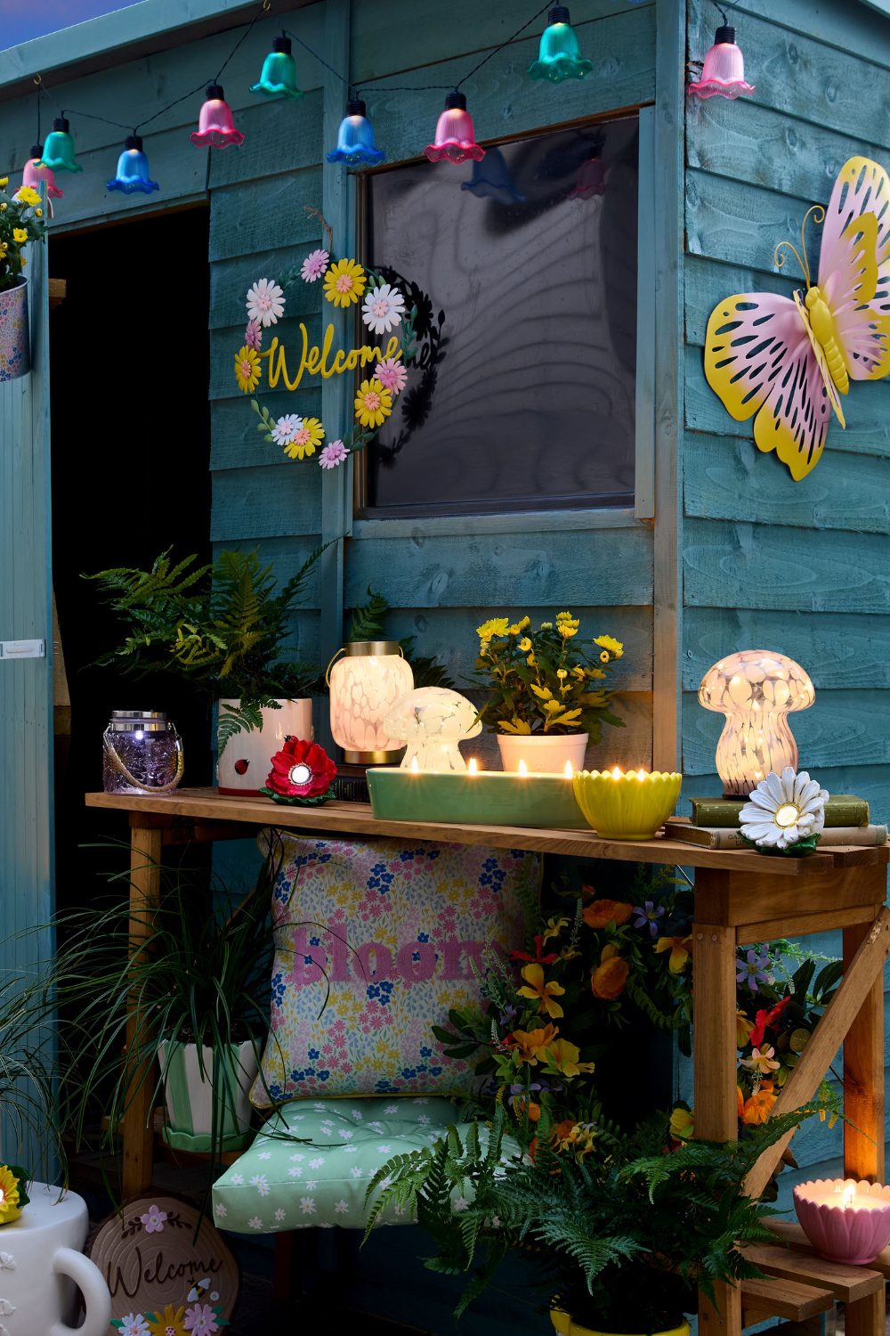 Blue garden shed with colourful string lights and wooden table of candles and lamps