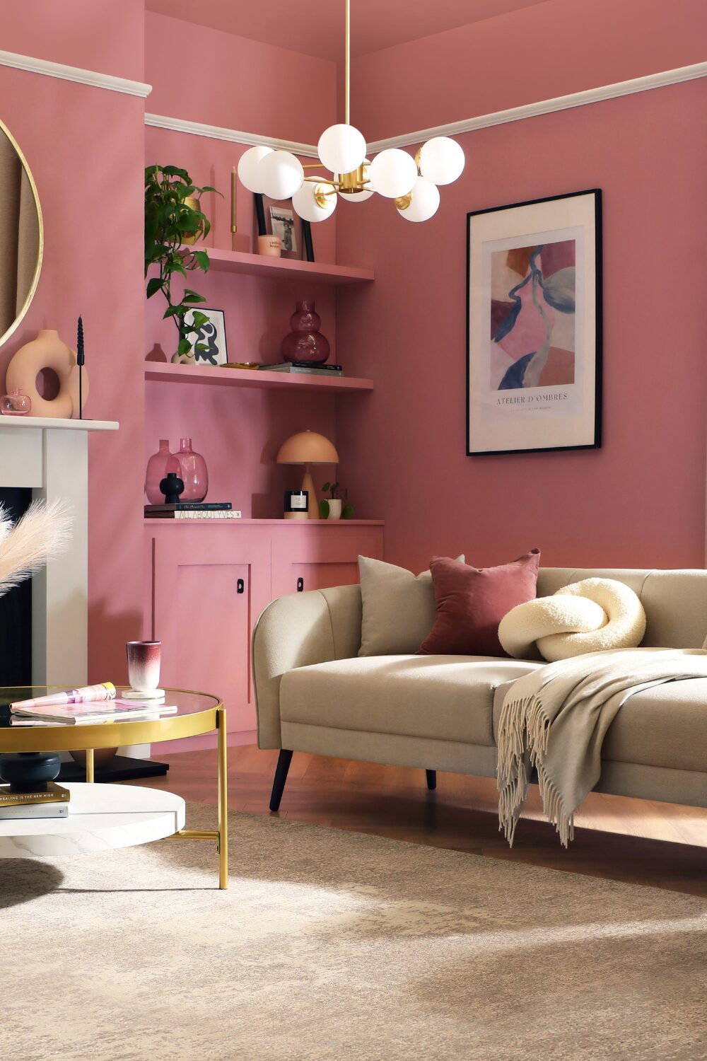 Pink living room with beige sofa, built-in shelves holding vases and books, and round glass table
