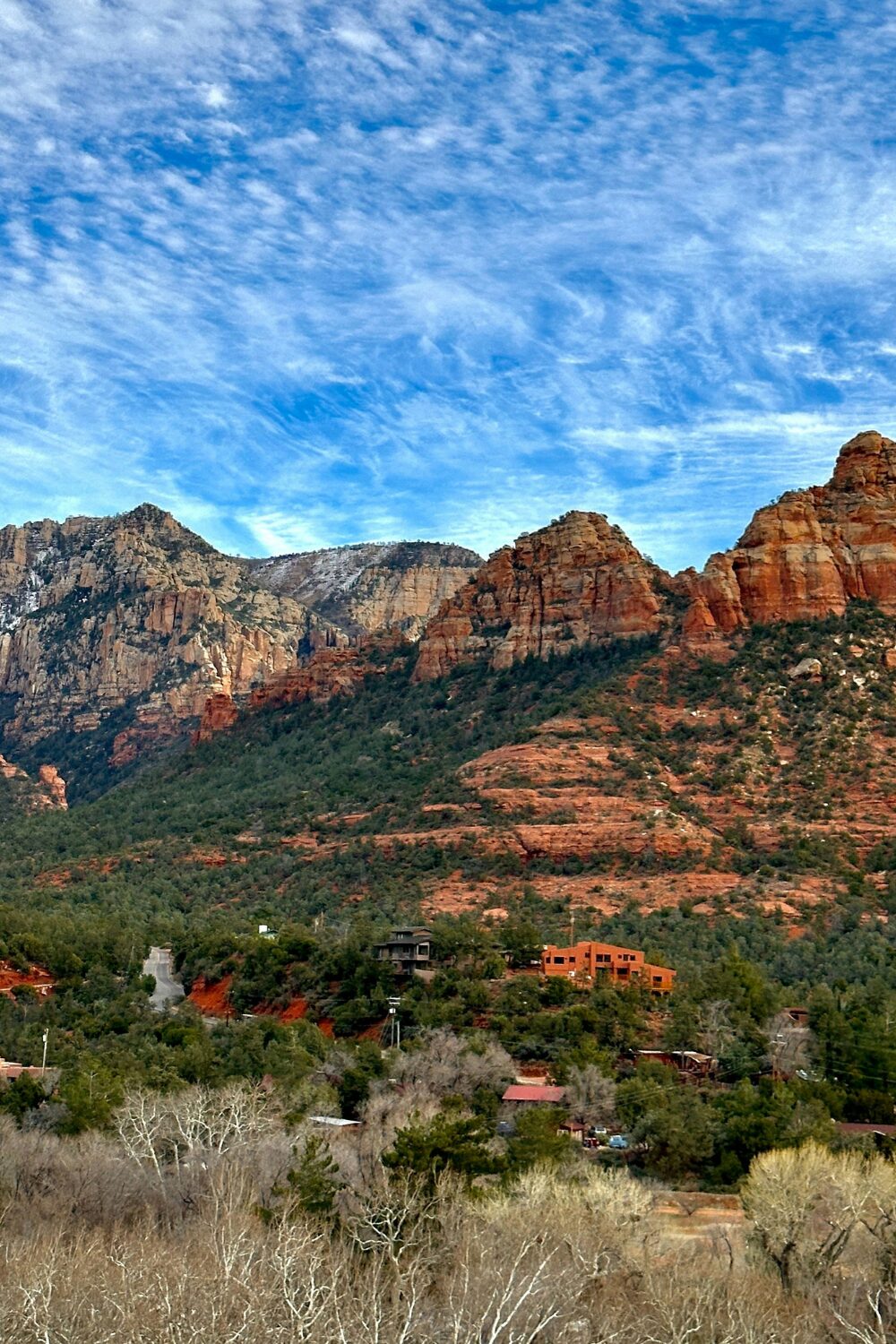 Red rock cliffs against blue sky with green trees and red houses