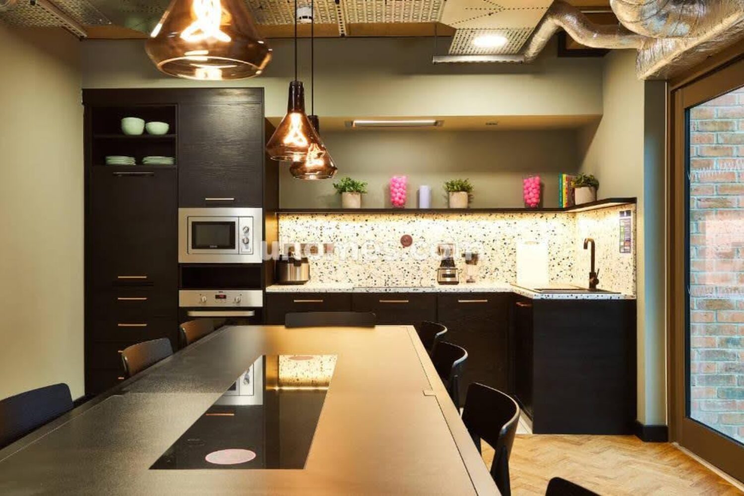Kitchen with dark cabinets, long dining table, and dappled splashback