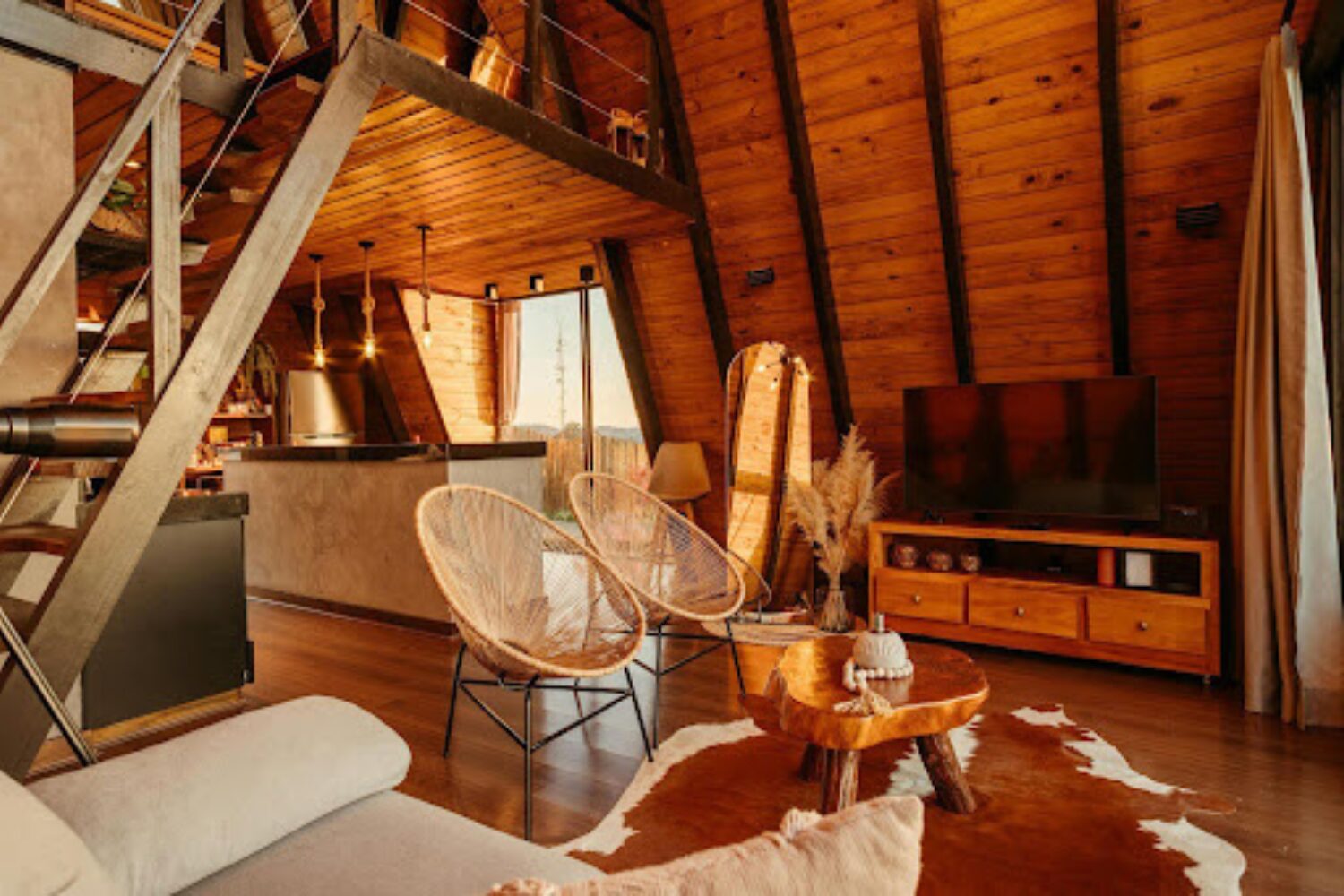 Wooden cabin with wicker chairs, TV on wooden stand, cowskin rug and stairs to upper level
