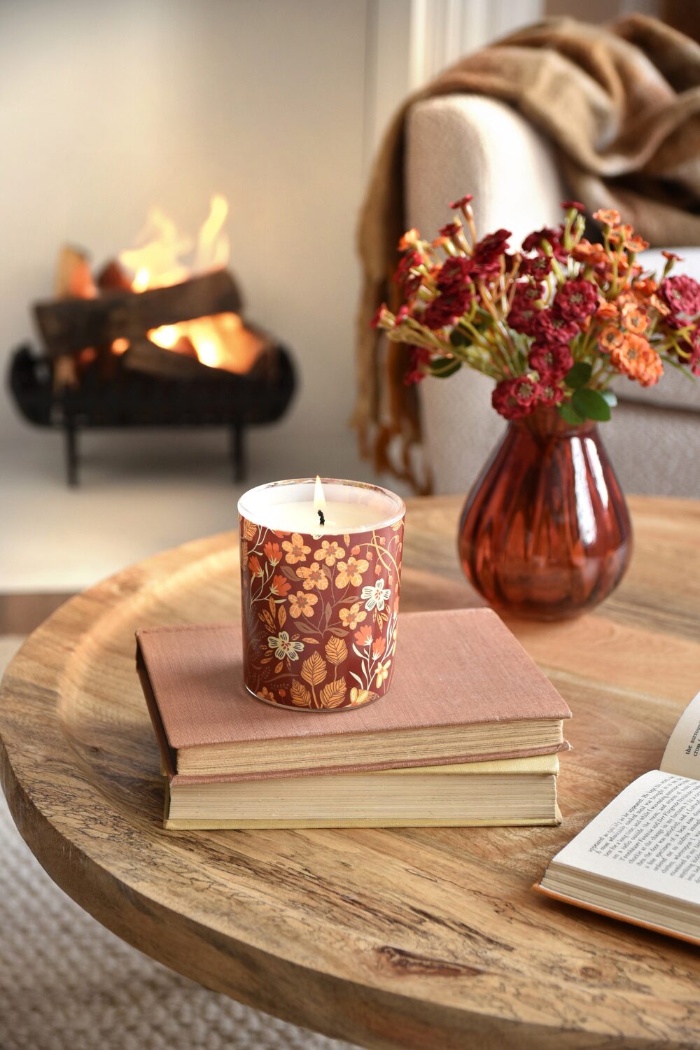 Round wooden table holding red books, vase and candle in front of open fireplace