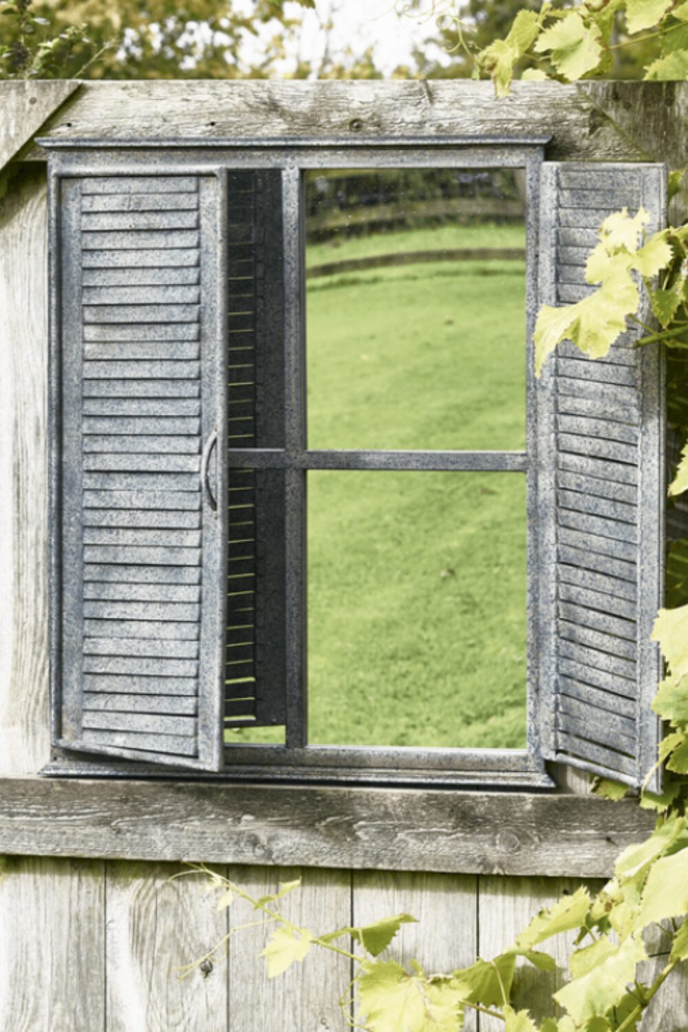 Mirror reflecting green lawn in wooden frame with shutters