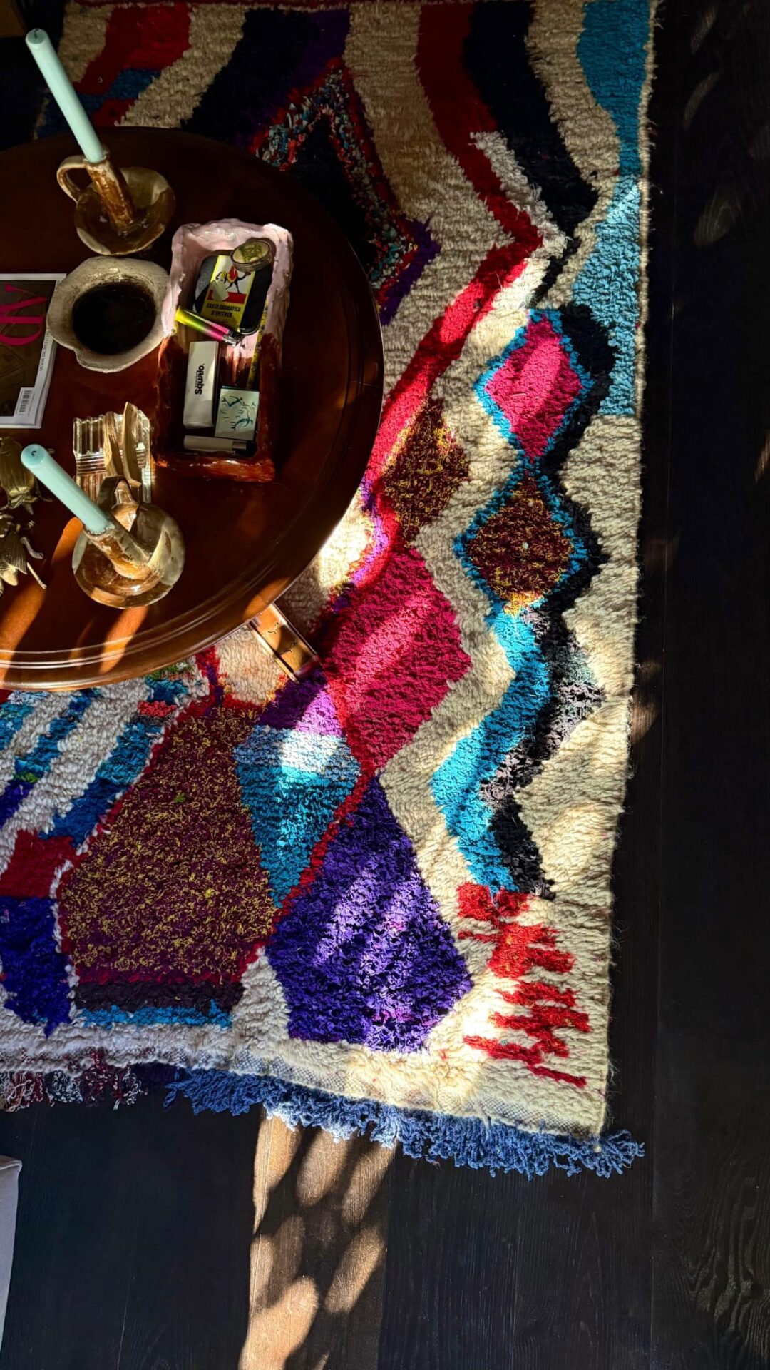 A jewel toned rug close up with wooden coffee table and candle with other paraphernalia