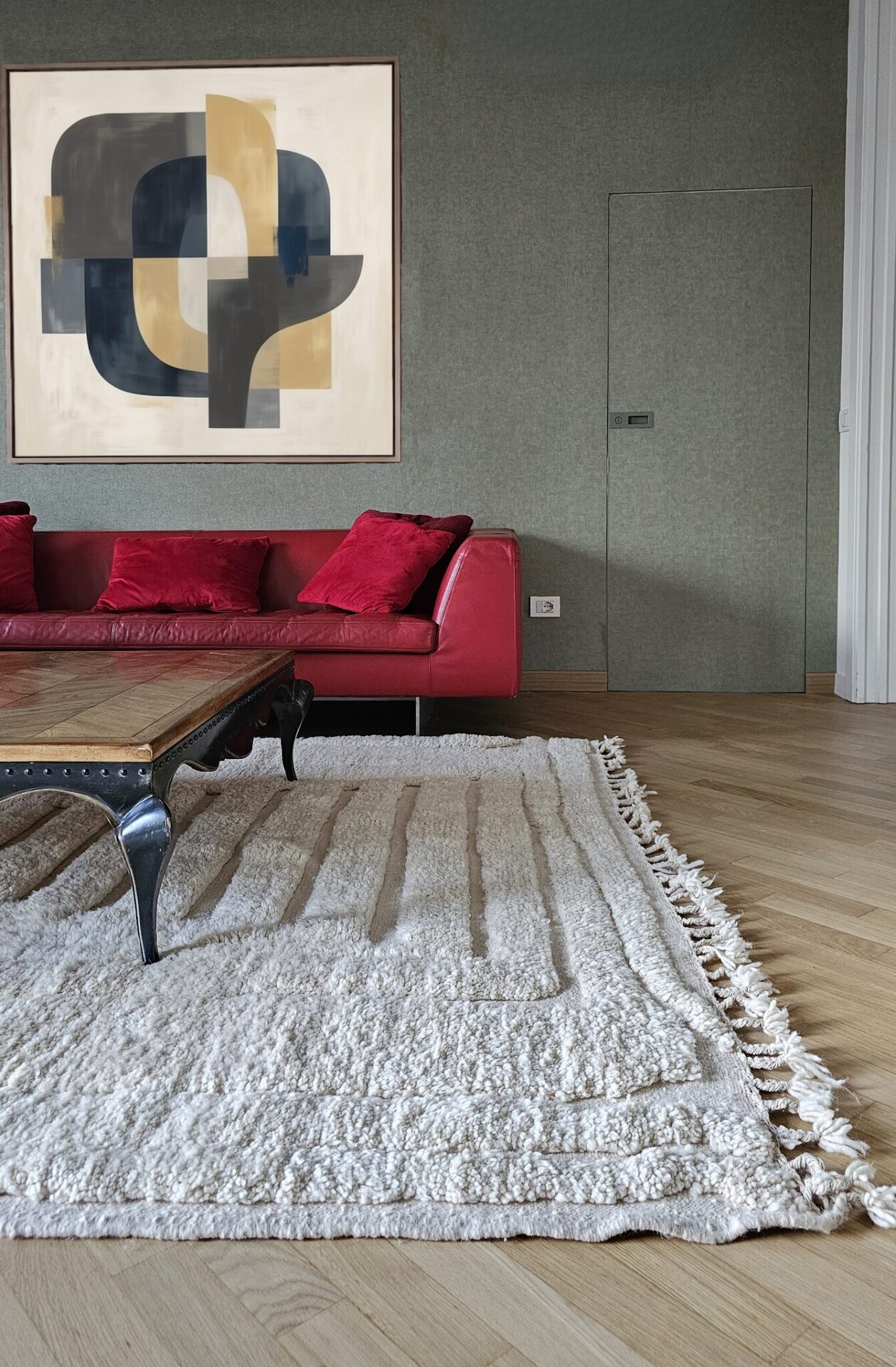 Living room with wooden floor and cream natural rug, wooden coffee table and red leather sofa. Green walls in the background