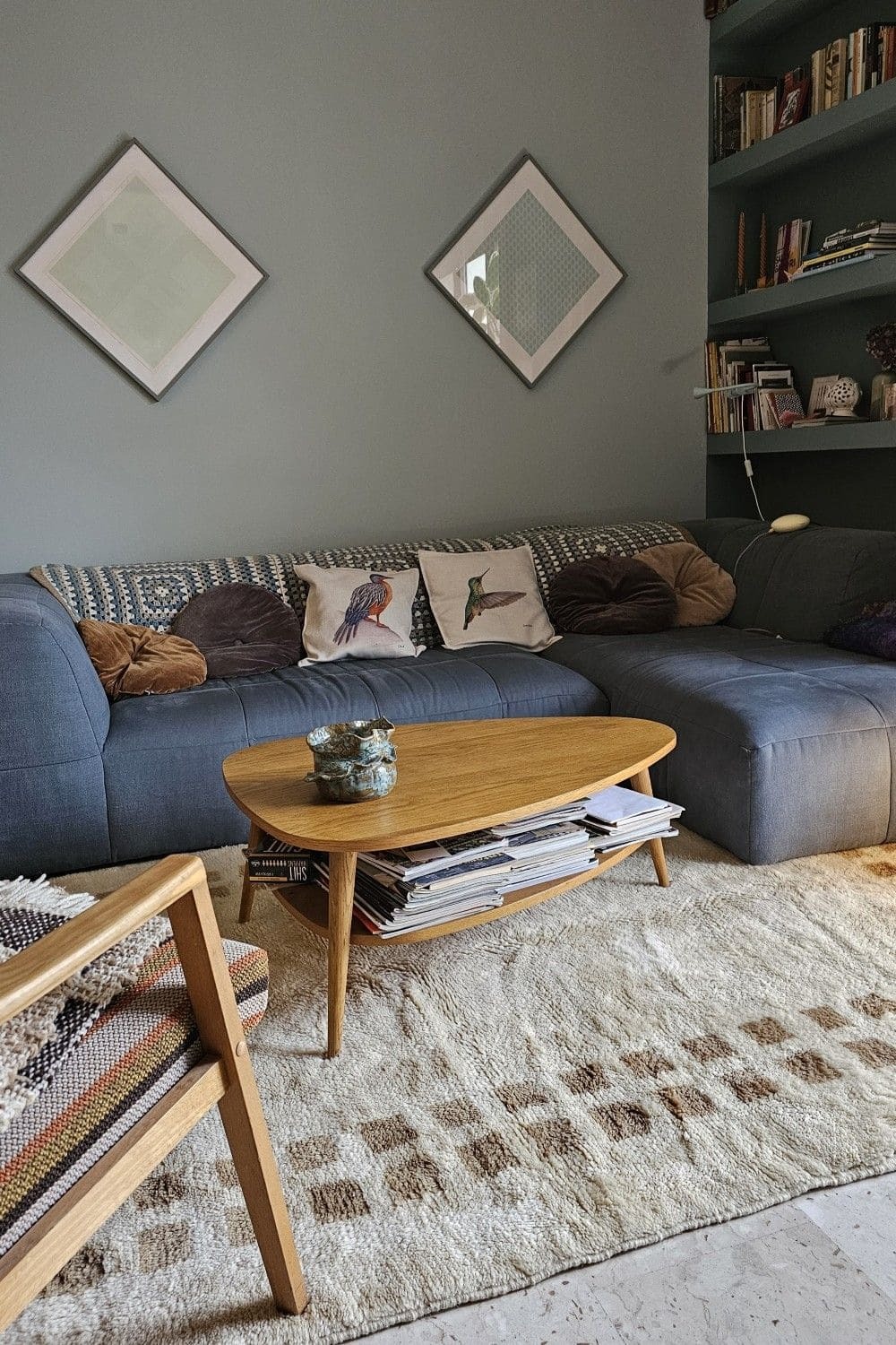 Corner blue comfy sofa with dark brown and neutral cushions, small oval wooden coffee table on a neutral cream and brown rug