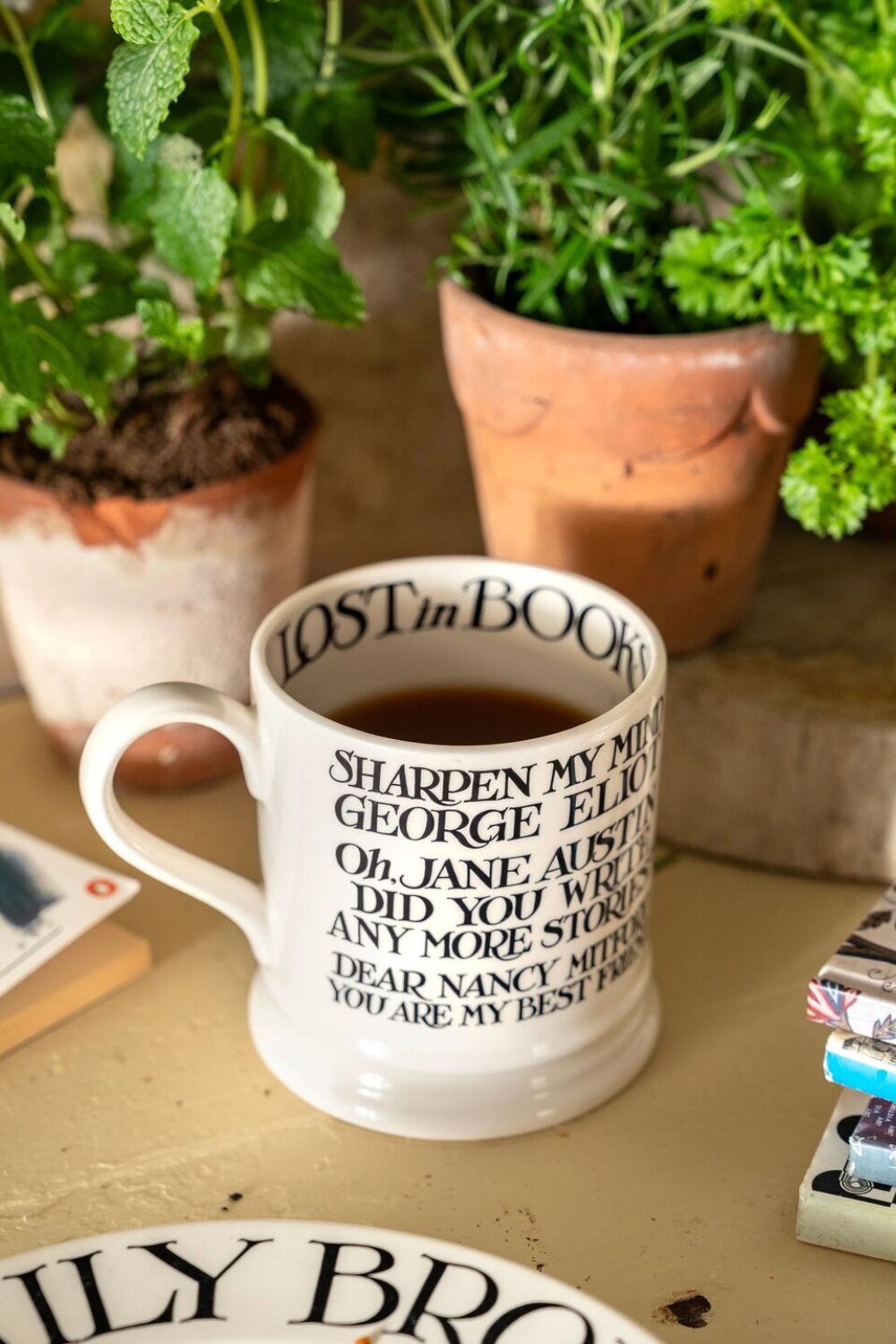 White mug and plate next to plant pots and book stack