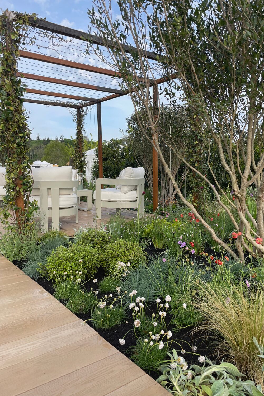 Lush garden with white chairs under metal pergola