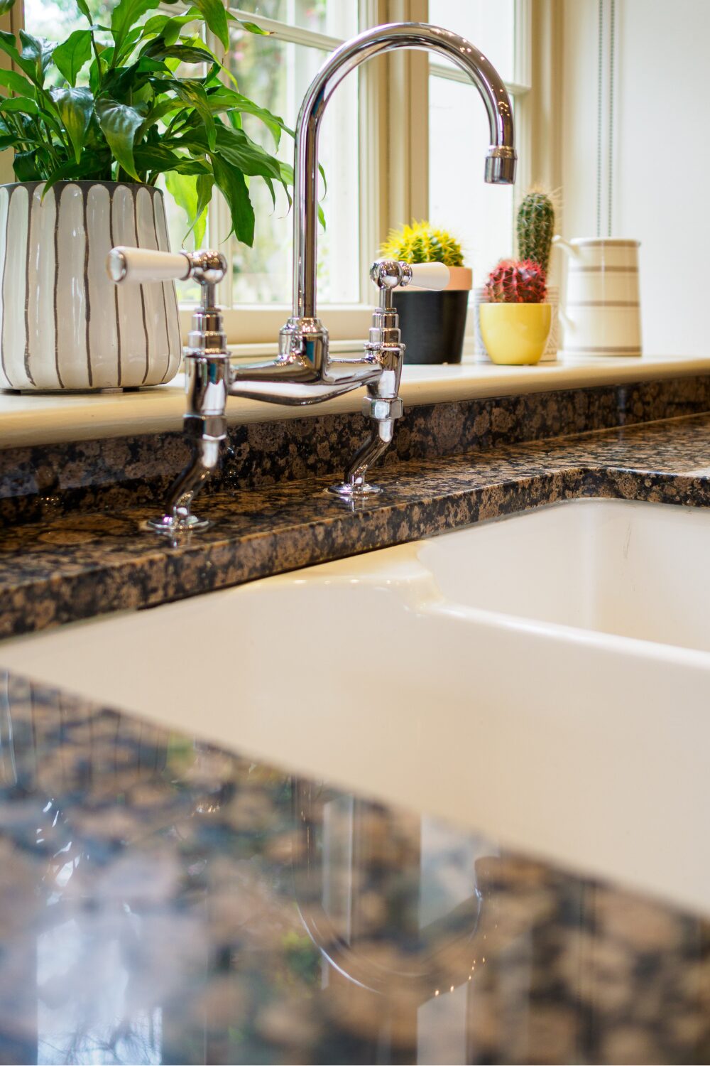 Silver kitchen tap on dark marbled counter with cacti pots on windowsill