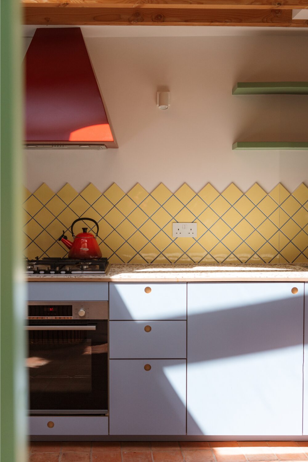 Kitchen with light blue cabinets, yellow tile backsplash, green shelves and red cooker hood