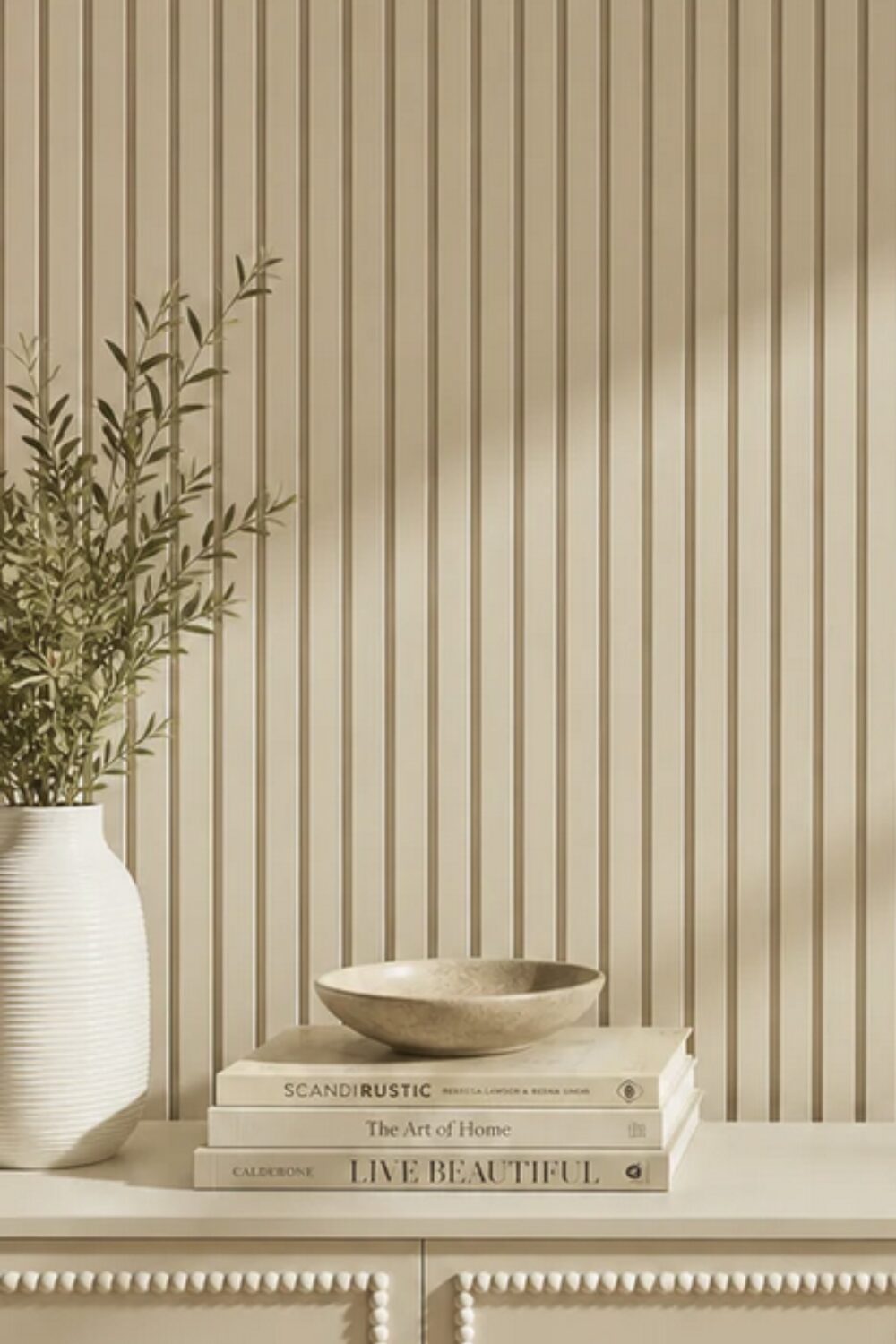 Cream cabinet with vase and books on top, in front of vertical slatted wall