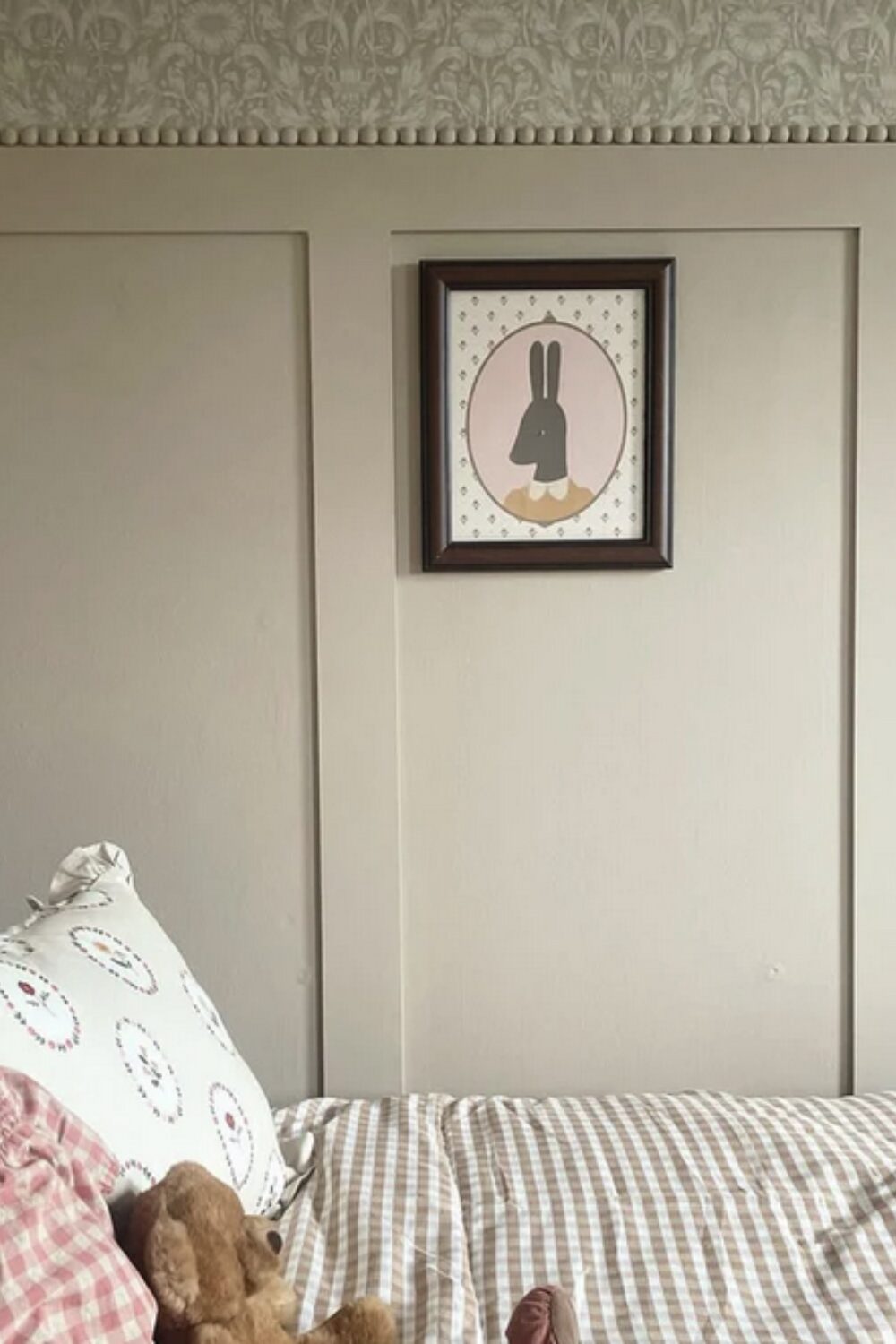 Bed with checked duvet in front of cream wood-panelled wall with framed rabbit print
