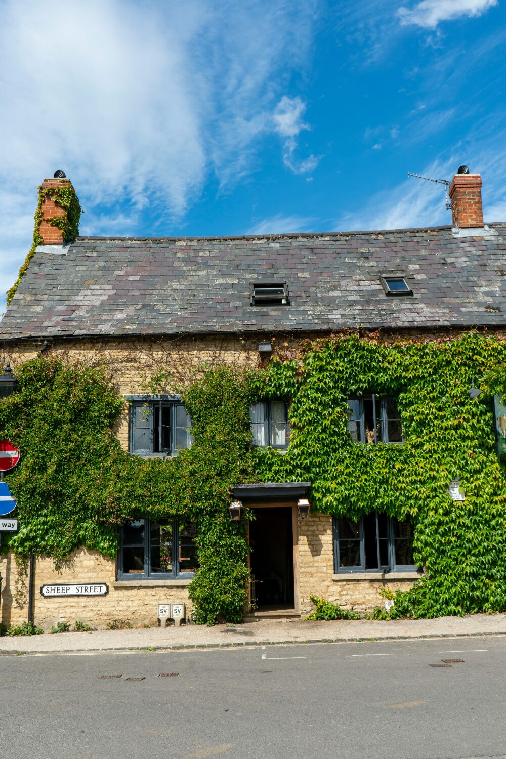 Yellow brick cottage with black roof covered in ivy