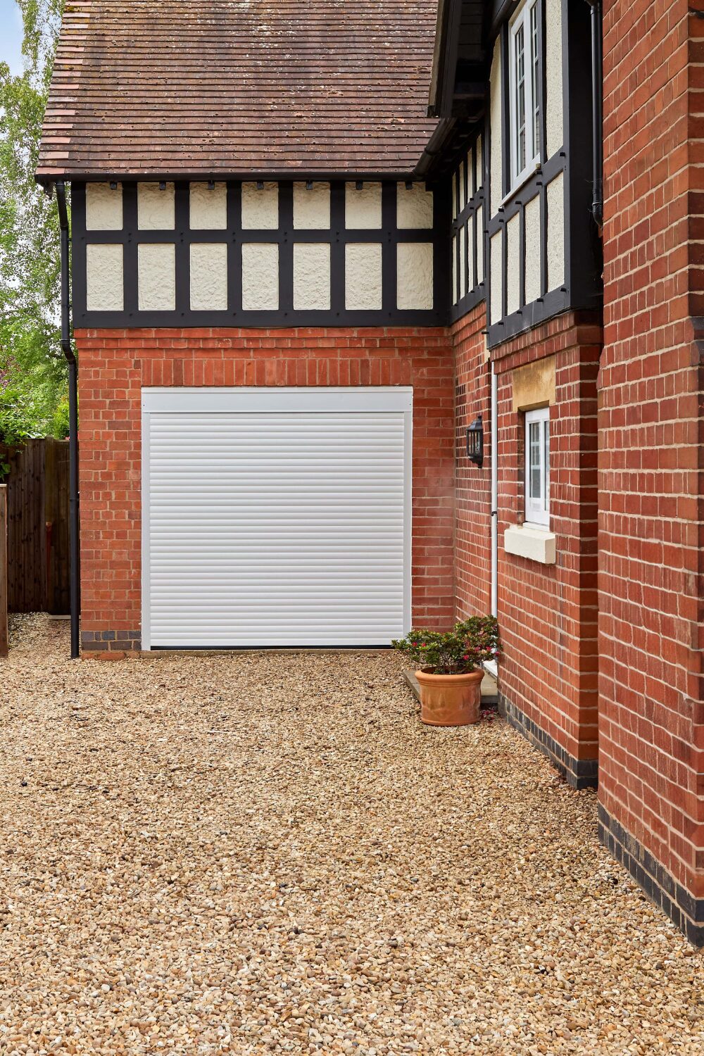 Exterior of red brick house with white garage door, timber-framed section and gravel drive