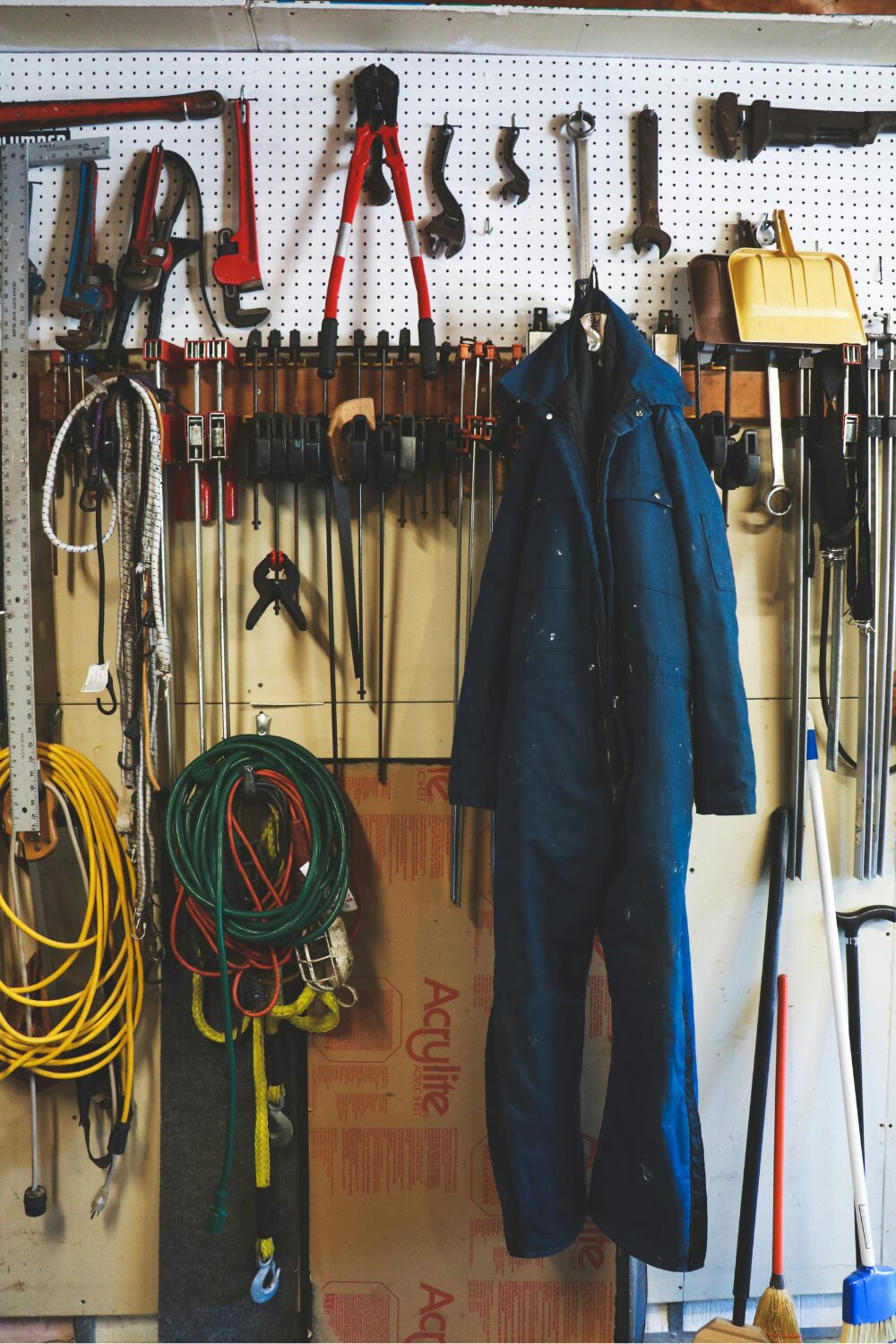 Garage workstation featuring hanging tools, blue coveralls, coiled wires, and brooms