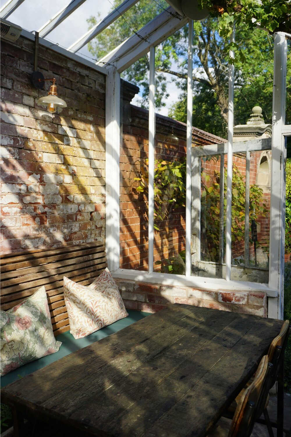 Wooden table with slatted bench inside conservatory attached to brick wall