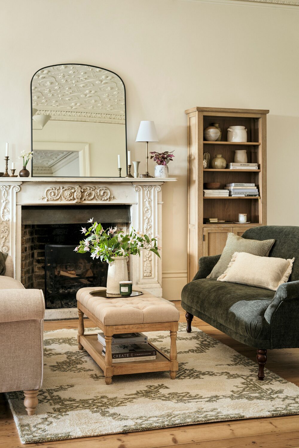 White living room with ornate fireplace, wooden cupboard and shelving unit, grey sofa and patterned rug
