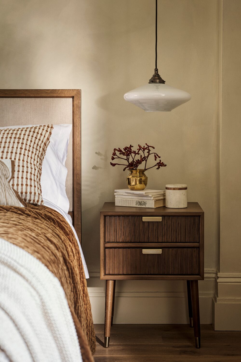 Brown bed next to wooden bedside table under hanging lamp